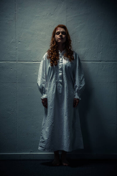 demonic woman in nightgown standing near wall