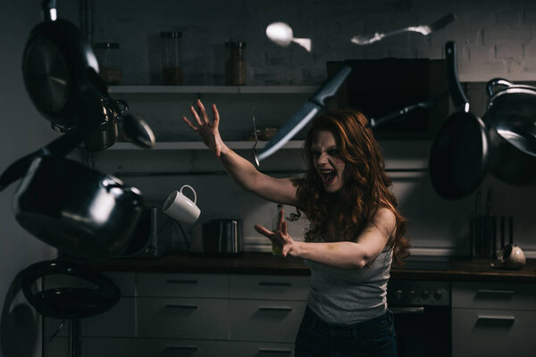 creepy yelling girl gesturing with levitating kitchenware in kitchen