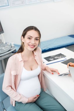 doctor showing ultrasound scan to happy pregnant woman in clinic clipart