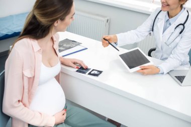 doctor showing digital tablet with blank screen to young pregnant woman with ultrasound scan clipart