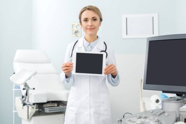 Profesyonel kadın doktor, klinikte ultrason tarayıcı ile boş ekranlı dijital tablet gösteriyor.