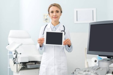 professional female doctor showing digital tablet with blank screens in clinic with ultrasound scanner clipart