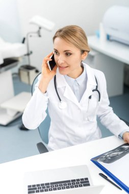 Güzel doktor ultrason taraması yapıyor ve klinikte akıllı telefondan konuşuyor. 