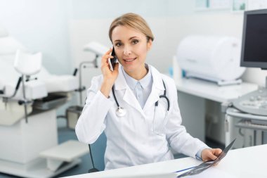 Profesyonel kadın doktor ultrason taraması yapıyor ve klinikte akıllı telefondan konuşuyor. 