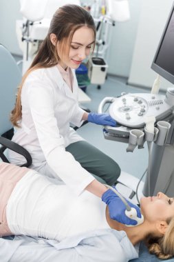 Gülümseyen doktor, klinikte ultrason taraması yapan kadın tiroidi inceliyor.