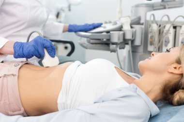 Doktor, klinikte ultrason taraması yapılan güzel bir hastanın midesini inceliyor. 