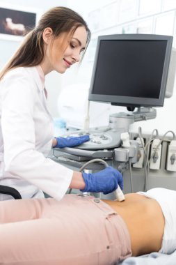 Genç doktor, klinikte ultrason taraması yapılan bir kadının midesini inceliyor. 