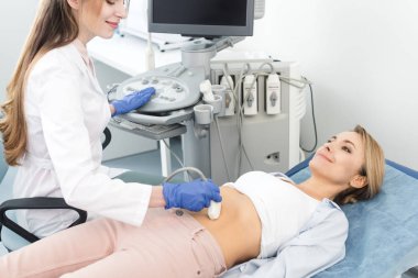 Gülümseyen güzel doktor, klinikte ultrason taramasıyla kadın hastanın midesini inceliyor. 