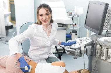 Gülümseyen genç doktor, klinikte ultrason taraması yapılan bayanın böbreğini inceliyor.  