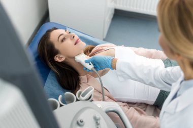 Doktor, klinikte ultrason taraması yapılan güzel bir hastanın tiroidini inceliyor.