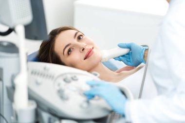 Doktor, klinikte ultrason taraması yapılan kadın hastanın tiroidini inceliyor.