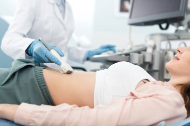 Klinikte ultrason taraması yapılan bir kadının midesini muayene eden doktor görüntüsü. 