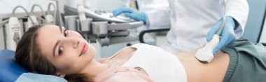 Doktorun, klinikte ultrason taramasıyla gülümseyen hastanın midesini muayene ettiği panoramik bir fotoğraf. 