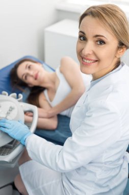 Gülümseyen doktor klinikte ultrason taraması yaptıran bayanın böbreğini inceliyor.  