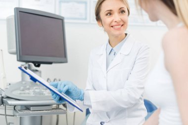 Gülümseyen doktor ultrason tarayıcısının yanındaki klinikteki hastaya teşhis koyuyor.