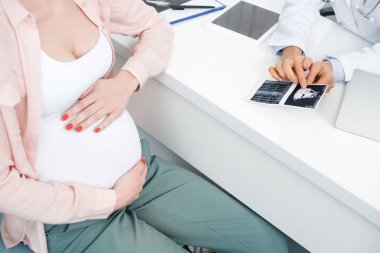 cropped view of doctor showing ultrasound scan to young pregnant woman touching belly clipart