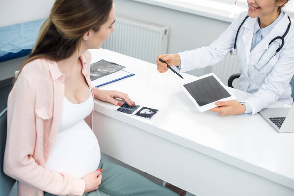 doctor showing digital tablet with blank screen to young pregnant woman with ultrasound scan