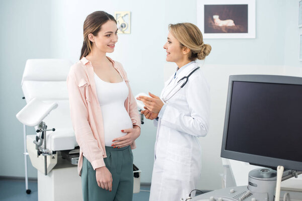 happy pregnant woman having consultation with smiling gynecologist in clinic