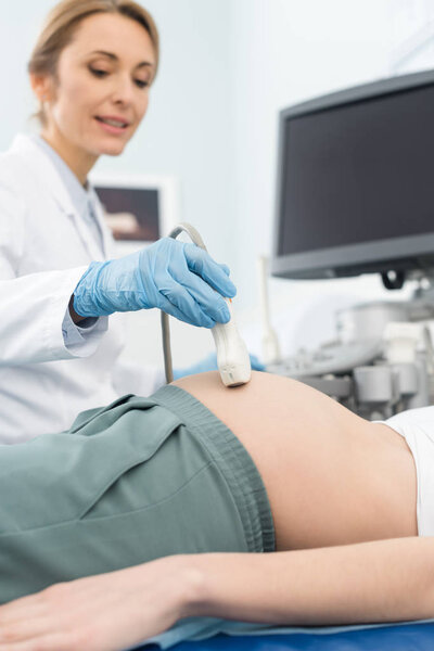 professional doctor examining belly of pregnant woman with ultrasound scan in clinic