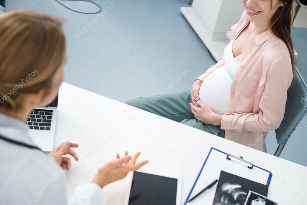 young happy pregnant woman having consultation with doctor in gynecological clinic