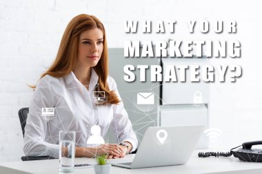 Çekici iş kadını dizüstü bilgisayarlı ve telefonlu masaya bakıyor. Pazarlama stratejiniz nedir?