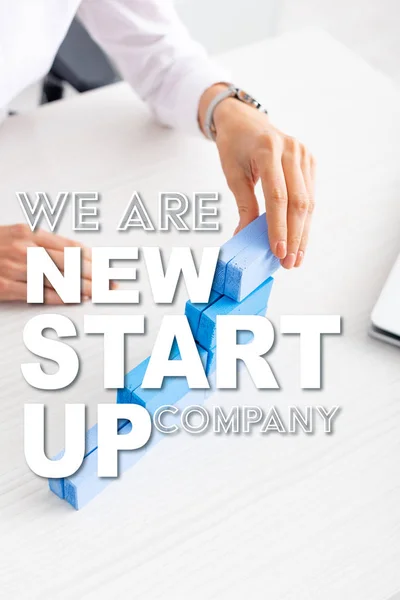Cropped view of businesswoman stacking blue building blocks near laptop on table, we are new startup company illustration — Stock Image Cropped View Businesswoman Stacking Blue Building Blocks Laptop Table New Stock Picture