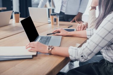Laptop kullanan ve çok kültürlü iş arkadaşlarıyla çalışan bir iş kadını görüşü.  