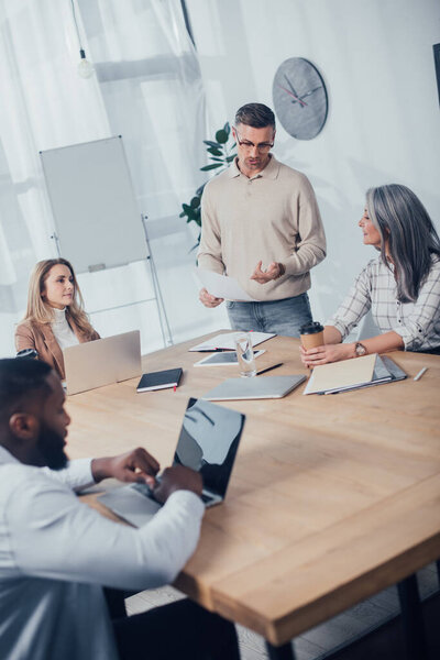 multicultural doing paperwork and talking during meeting in creative agency 