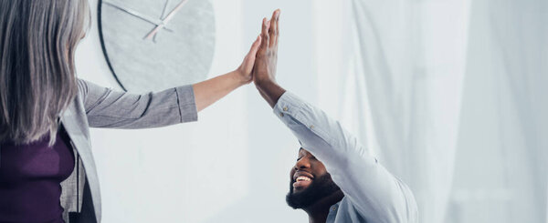 panoramic shot of smiling multicultural colleagues giving high five in office  