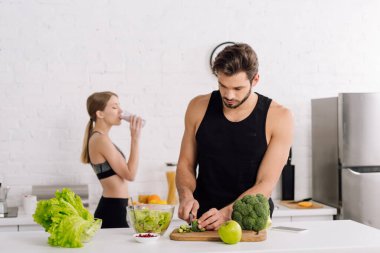 Yakışıklı bir adamın, kızın yanında yemek pişirip smoothie içtiği seçici odak noktası. 