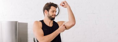 panoramic shot of handsome and sportive man measuring muscle on hand  clipart