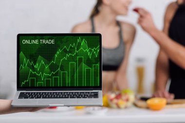 Bilgisayarın seçici odağı. Mutfakta kadın ve erkeğin yanında çevrimiçi ticaret ekranda. 