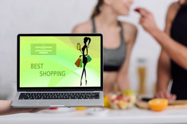 En iyi alışveriş sitesi olan dizüstü bilgisayarın seçici odağı mutfaktaki çiftin yanında ekranda 