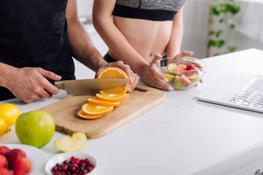 Kadının, salatanın ve dizüstü bilgisayarın yanında turuncu kesen adam görüntüsü 