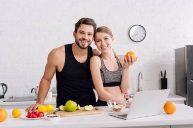 Meyve ve laptopun yanında spor giyim sektöründe neşeli serbest çalışanlar 