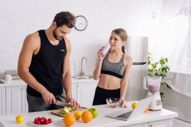 Sportif kız, mutfakta yemek yapan adamın yanında smoothie içiyor. 