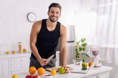 Mutfakta blender ve dizüstü bilgisayarın yanında yemek pişiren mutlu adam. 
