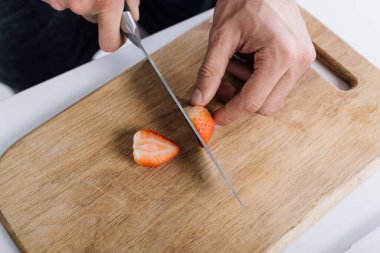 cropped view of man cutting red organic strawberry on chopping board  clipart