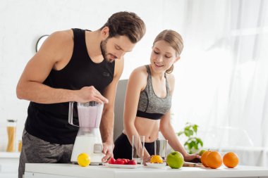 sportive man preparing smoothie near happy girl and fruits  clipart