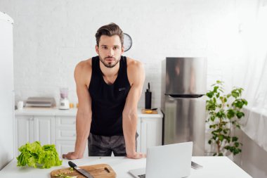 Laptopun yanında yakışıklı bir adam ve doğrama tahtasının yanında yeşil marul. 