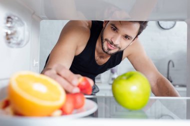 Buzdolabından çilek alan yakışıklı bir adamın seçici odağı. 