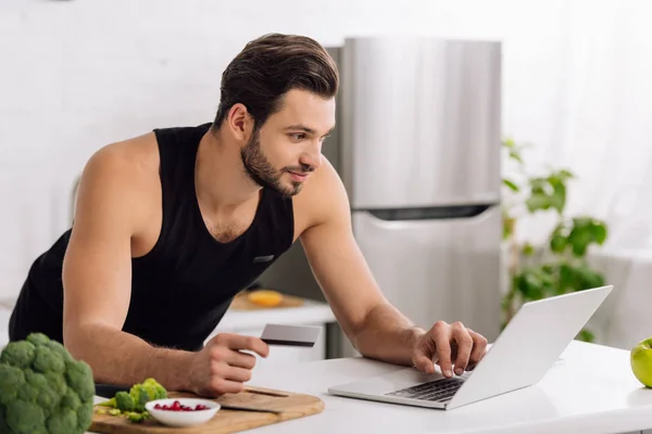 Pohledný Muž Držící Kreditní Kartu Při Použití Notebooku Kuchyni — Stock fotografie