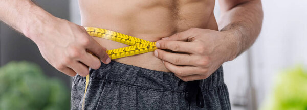 panoramic shot of shirtless man measuring waist 