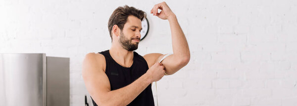 панорамный снимок красивого и спортивного мужчины, измеряющего мышцы на руках
 