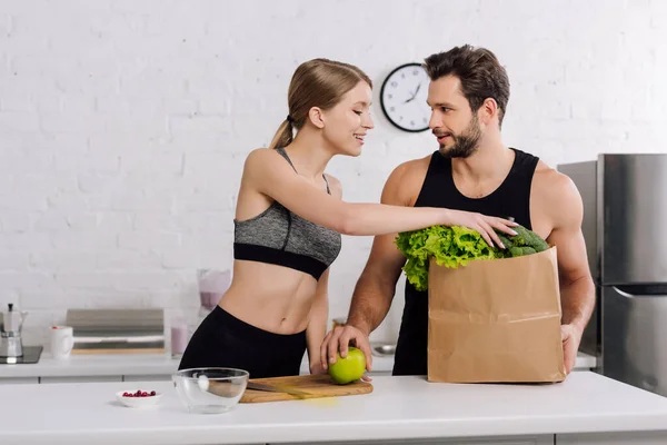 Menina Alegre Levando Alface Saco Papel Perto Homem Barbudo Cozinha — Fotografia de Stock