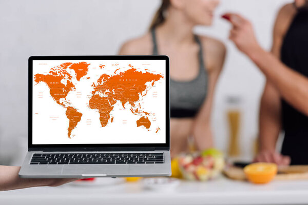 селективный фокус ноутбука с картой мира на экране рядом с парой на кухне
 