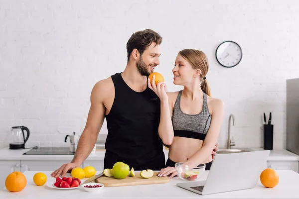 Menina Feliz Com Laranja Perto Homem Esportivo Laptop Frutas Cozinha — Fotografia de Stock