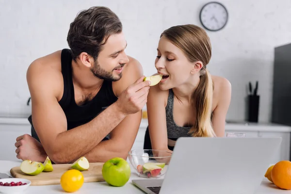 Feliz Hombre Alimentación Chica Con Rodajas Manzana Cerca Computadora Portátil —  Fotos de Stock