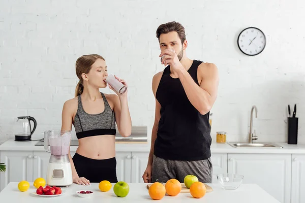 sportive man and woman drinking tasty smoothie near fruits
