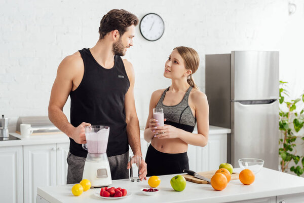 handsome man holding blender near happy woman and fruits 